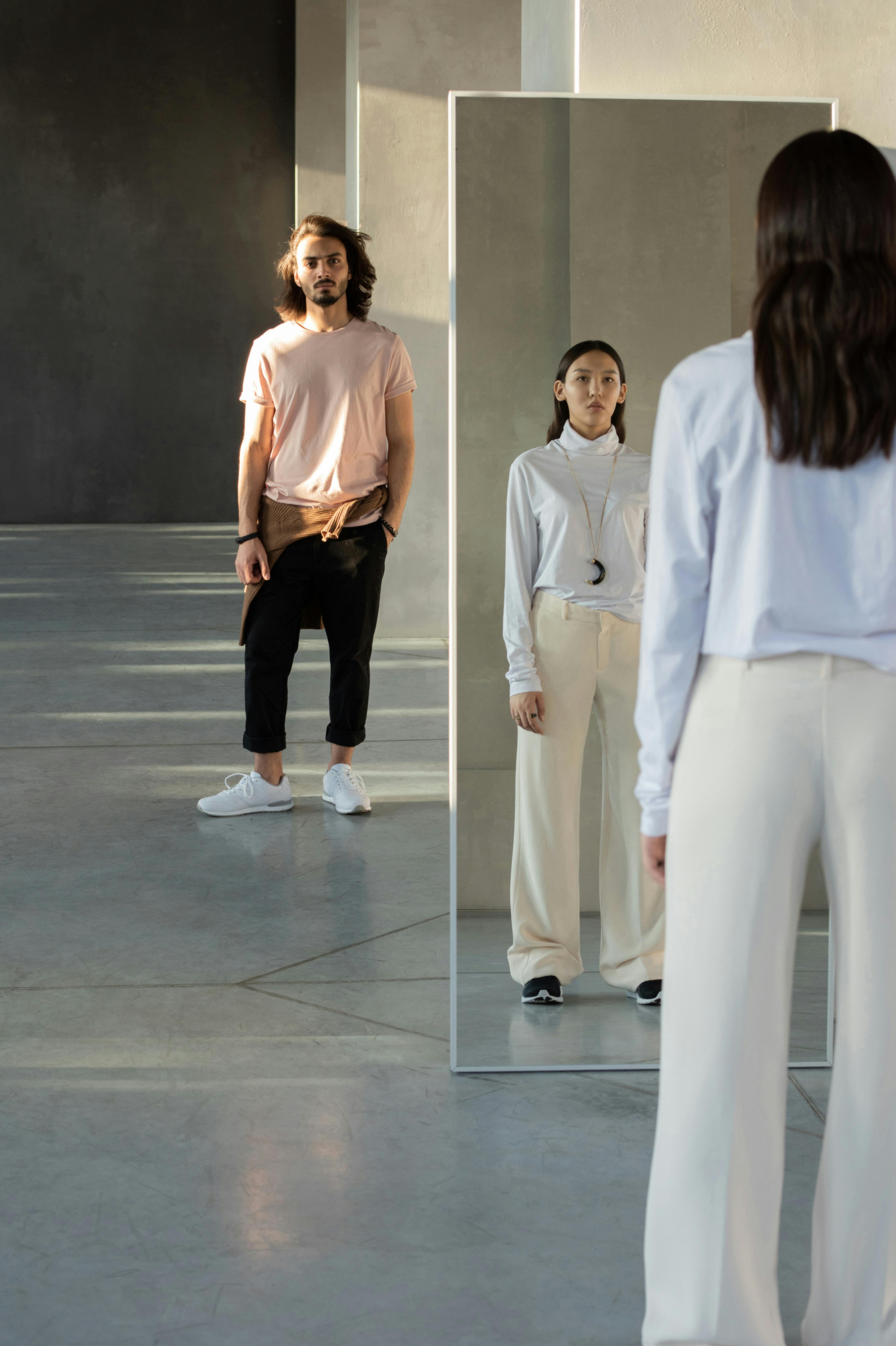 woman in white bluish long sleeve shirt and white pants standing in front of a mirror