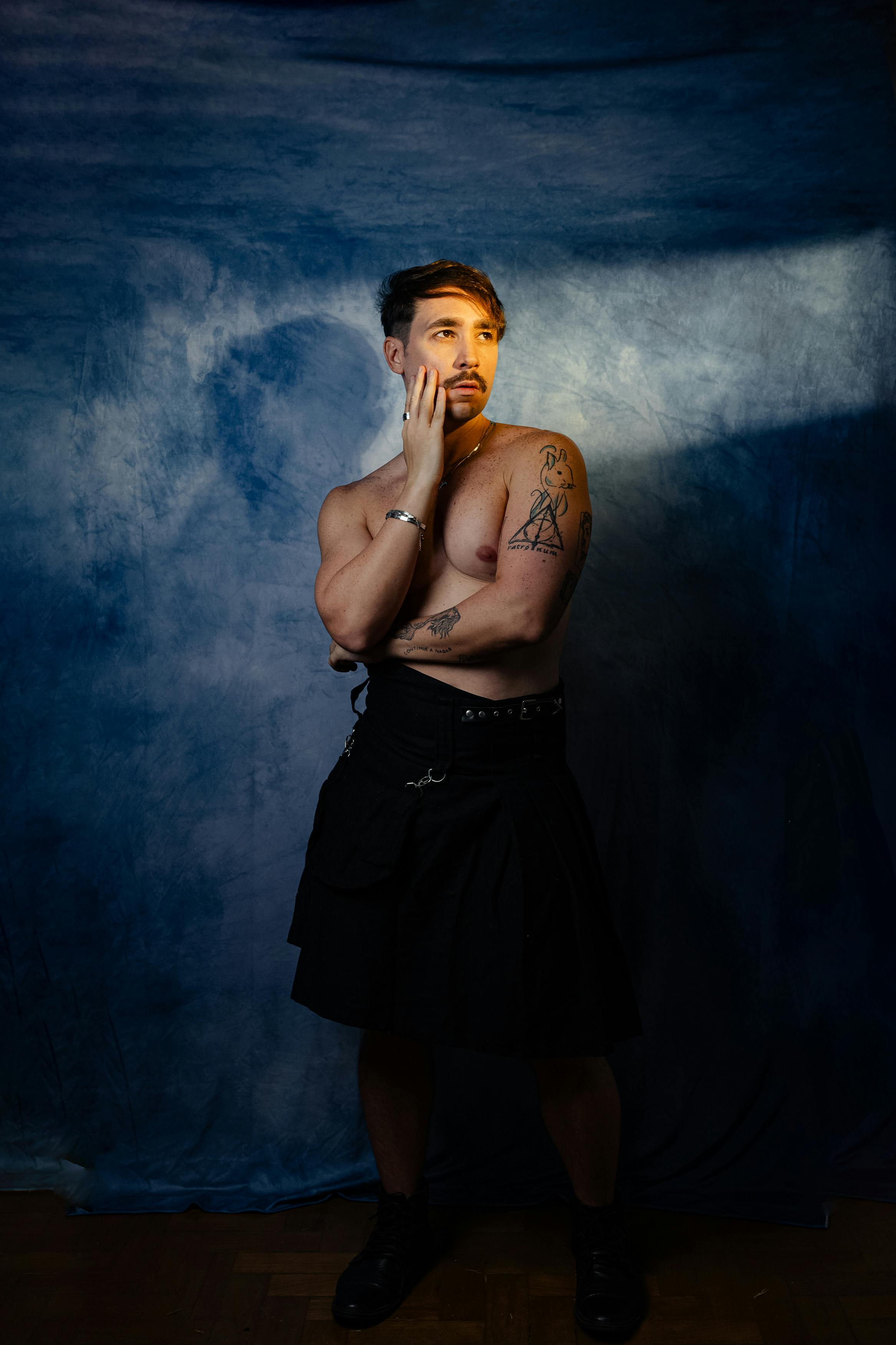 Portrait of a stylish tattooed man posing confidently against a dramatic dark blue backdrop.
