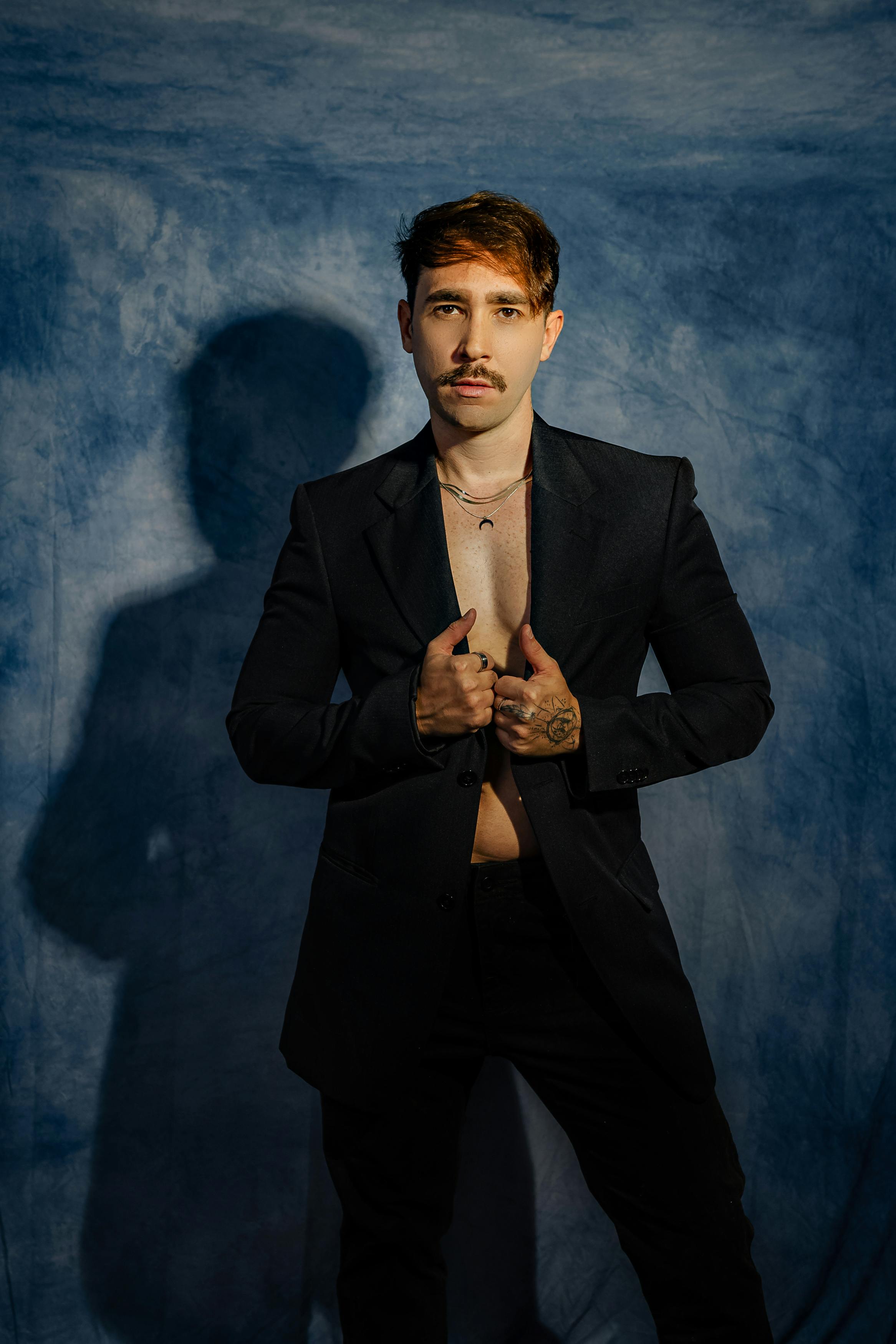 Portrait of a stylish man in a dark suit against a dramatic blue backdrop, showcasing modern fashion and elegance.