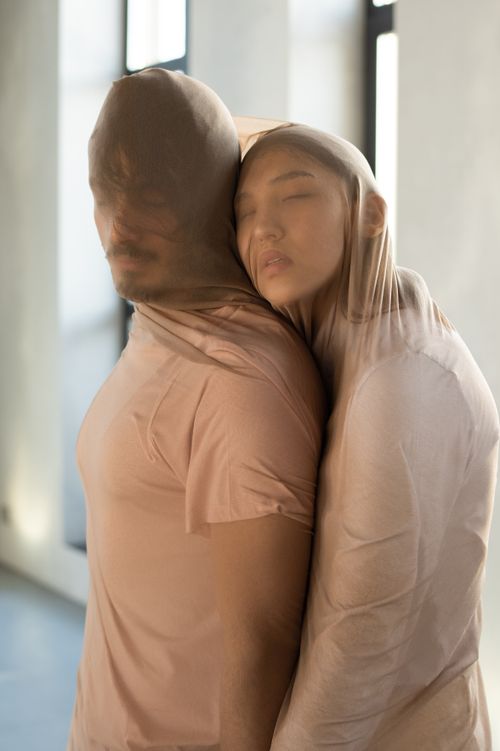 Free A couple embraces affectionately, their heads covered with sheer fabric, symbolizing connection and intimacy. Stock Photo