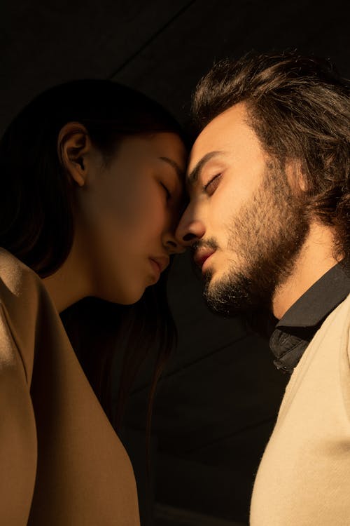 Close-up Photo of Couple with Their Eyes Closed Facing Each Other In Front of Dark Background