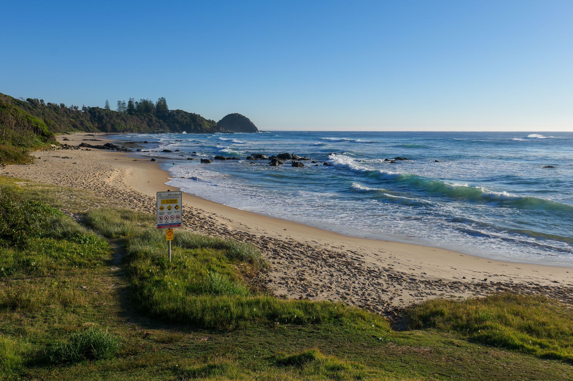 Peaceful scene of Shelly Beach with rolling waves and clear blue sky.
