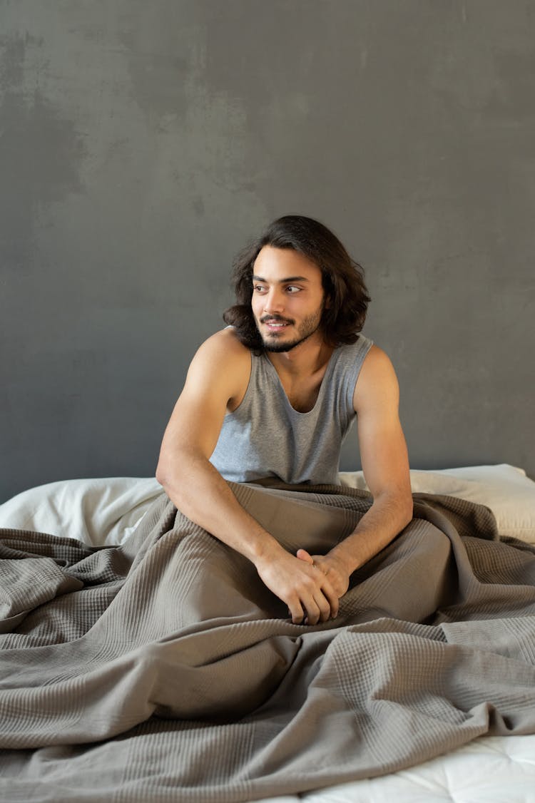 Man In Gray Tank Top Sitting On Bed