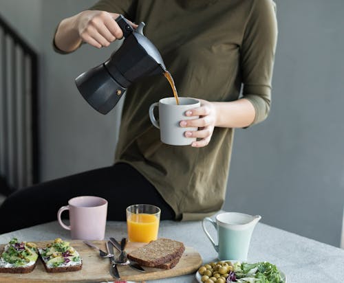Free Woman in Green Top Pouring Coffee in a White Mug Stock Photo