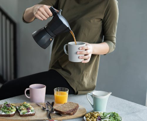 Woman in Green Top Pouring Coffee in a White Mug