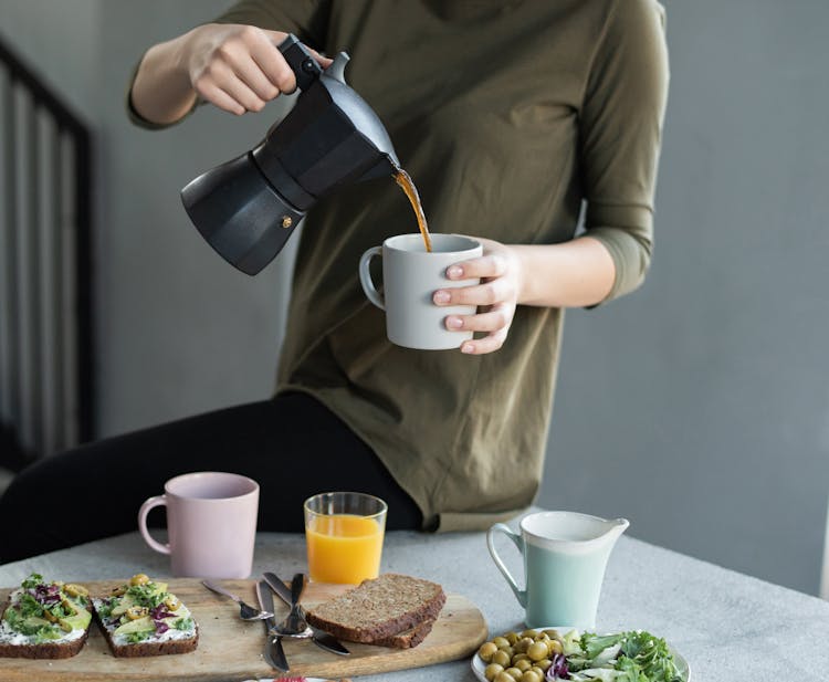 Woman In Green Top Pouring Coffee In A White Mug