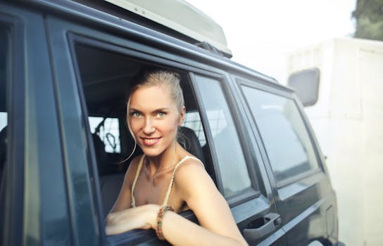 公路旅行中，一名身穿夏装的女子面带微笑，坐在汽车后座上，透过敞开的车窗望向镜头