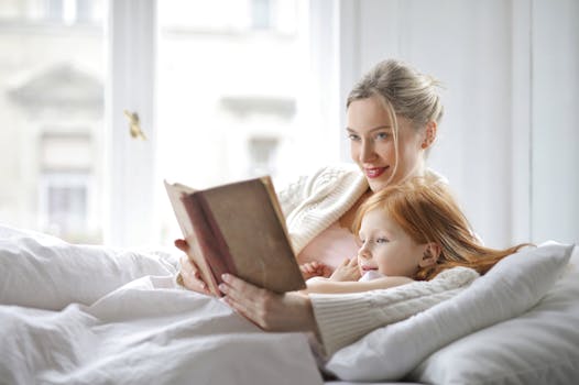 A mother and daughter enjoying a cozy moment reading together in a bright bedroom.