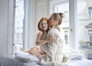 一位母亲在明亮的窗前深情地拥抱女儿，在室内分享温柔的时刻