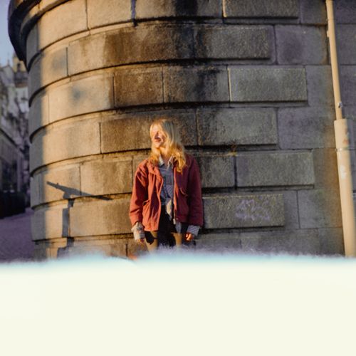 Free A young woman stands against a sunlit stone wall in Porto, Portugal, capturing a relaxed urban moment. Stock Photo