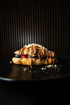 Close-up of a churro waffle topped with Nutella and fresh berries on a black plate.