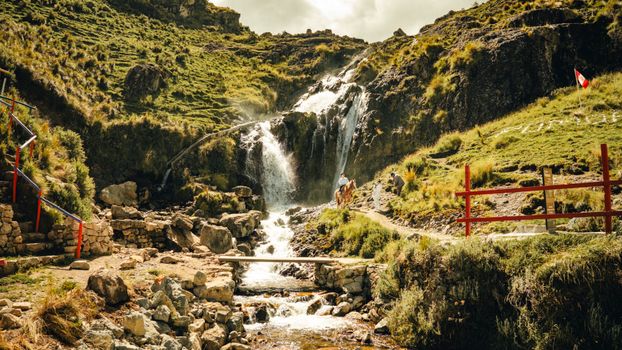 Picturesque waterfall with lush greenery in the mountains of Peru, featuring hikers and scenic trails.