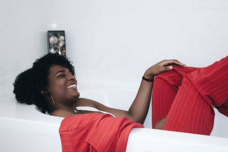 Photo Of Laughing Woman In Red Pinstripe Suit Lying Inside Bathtub