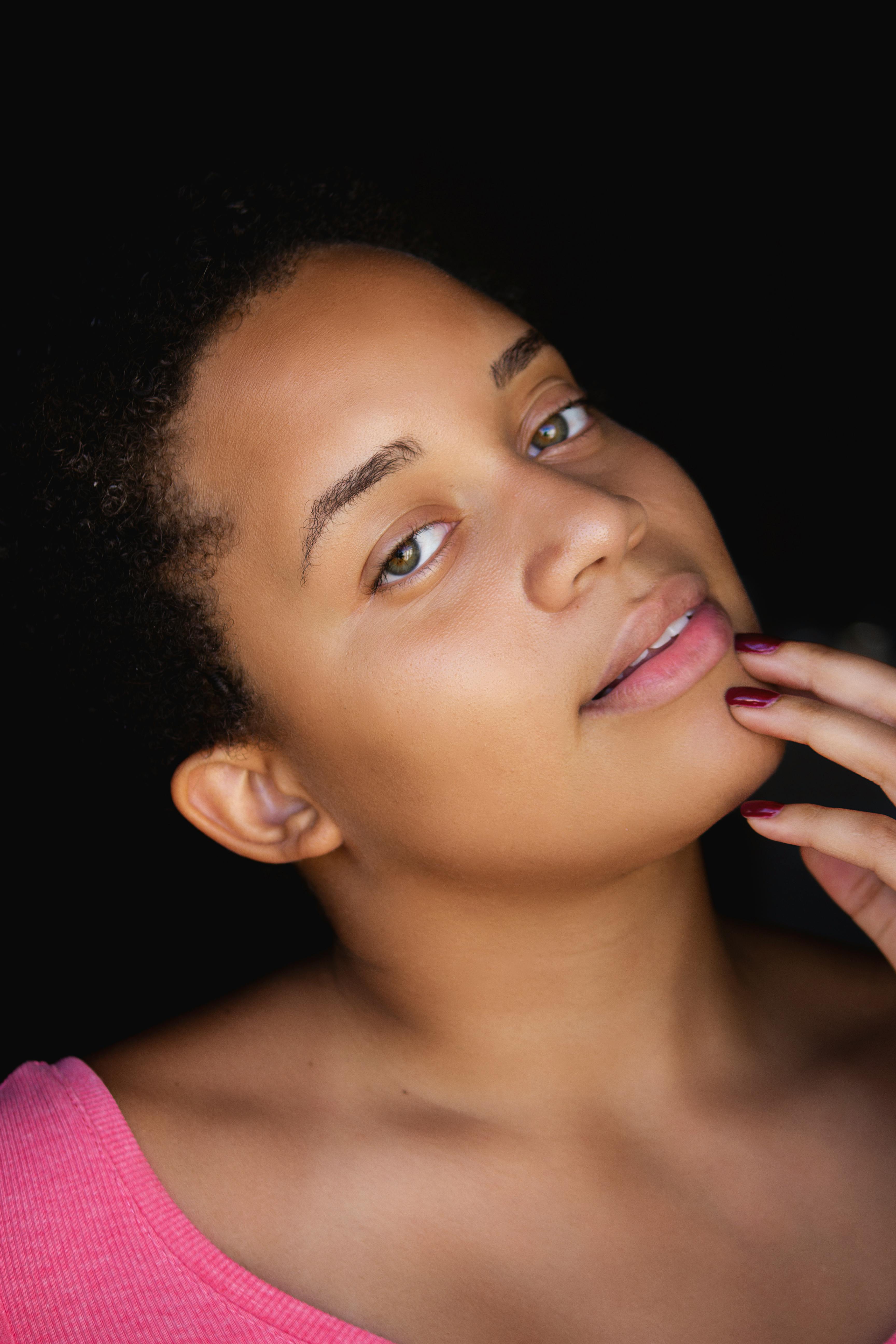 Elegant close-up portrait of a woman wearing a pink top against a black background, showcasing natural beauty and casual style.