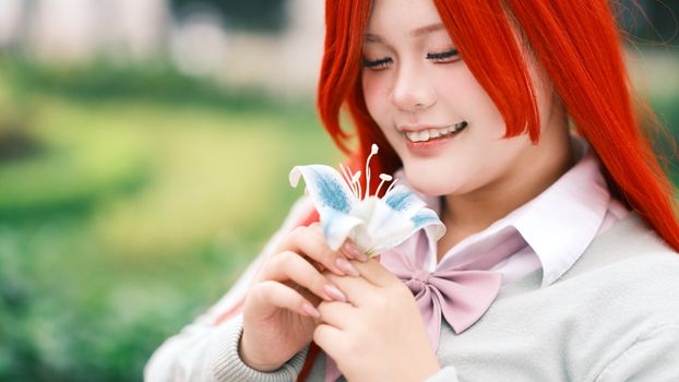Red-haired cosplayer with anime-inspired look holding a lily flower outdoors in vibrant setting.