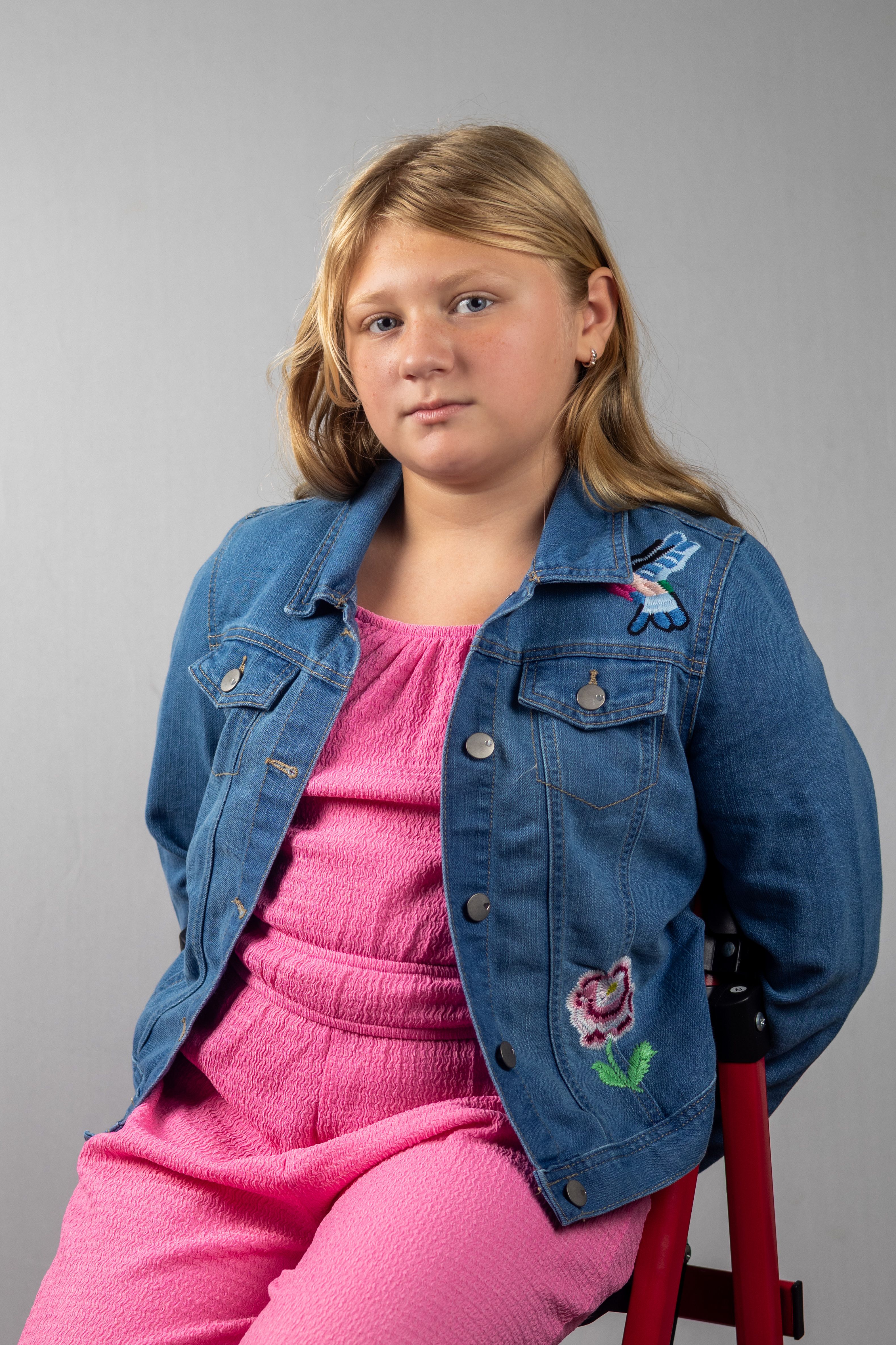 A young girl in a denim jacket sits confidently against a neutral background.