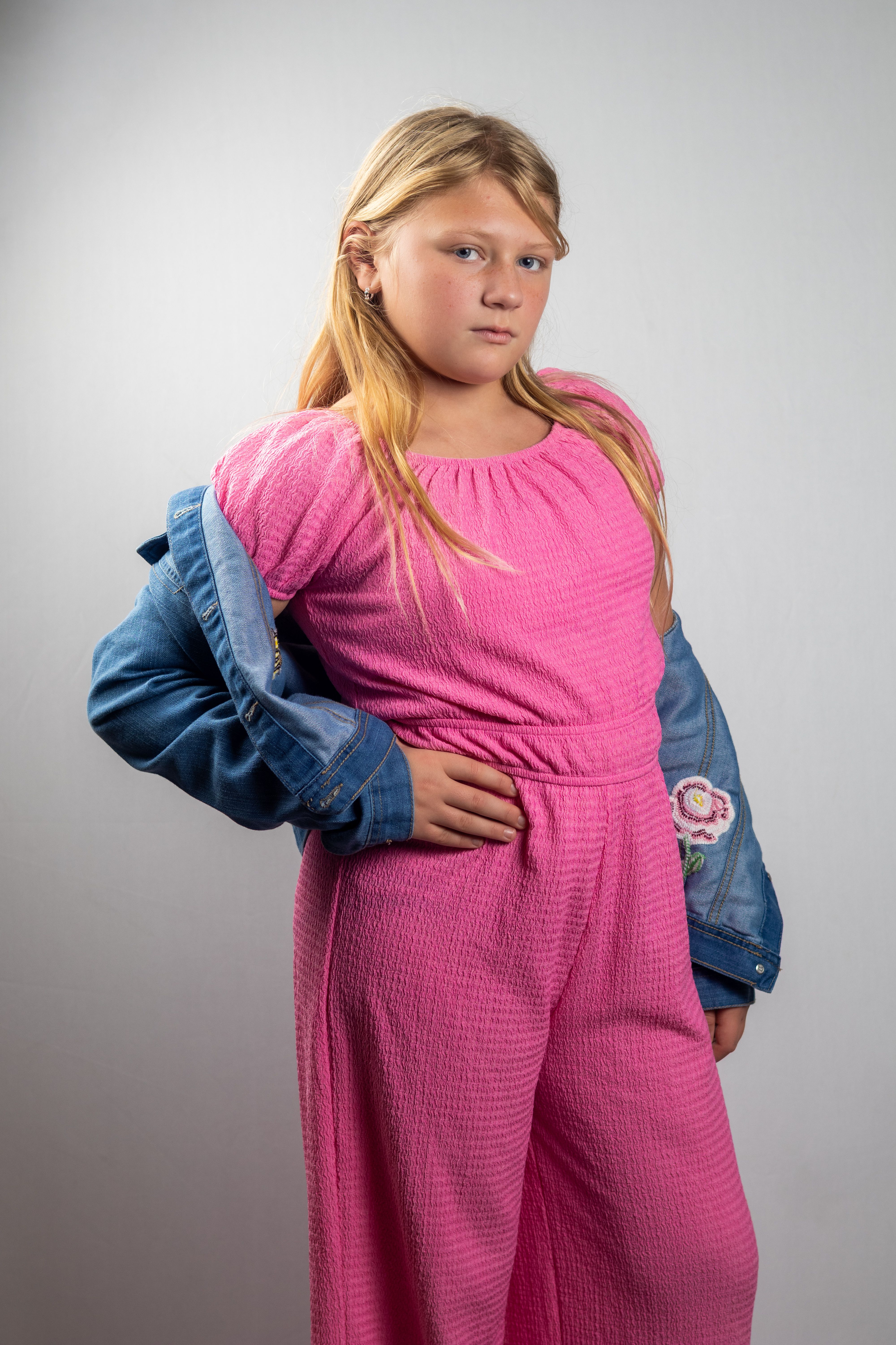 Young girl posing confidently in a pink outfit with a denim jacket, perfect for fashion and lifestyle content.