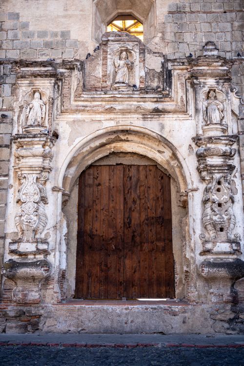 Free Rustic stone archway with wood door and sculptures in Antigua Guatemala. Stock Photo
