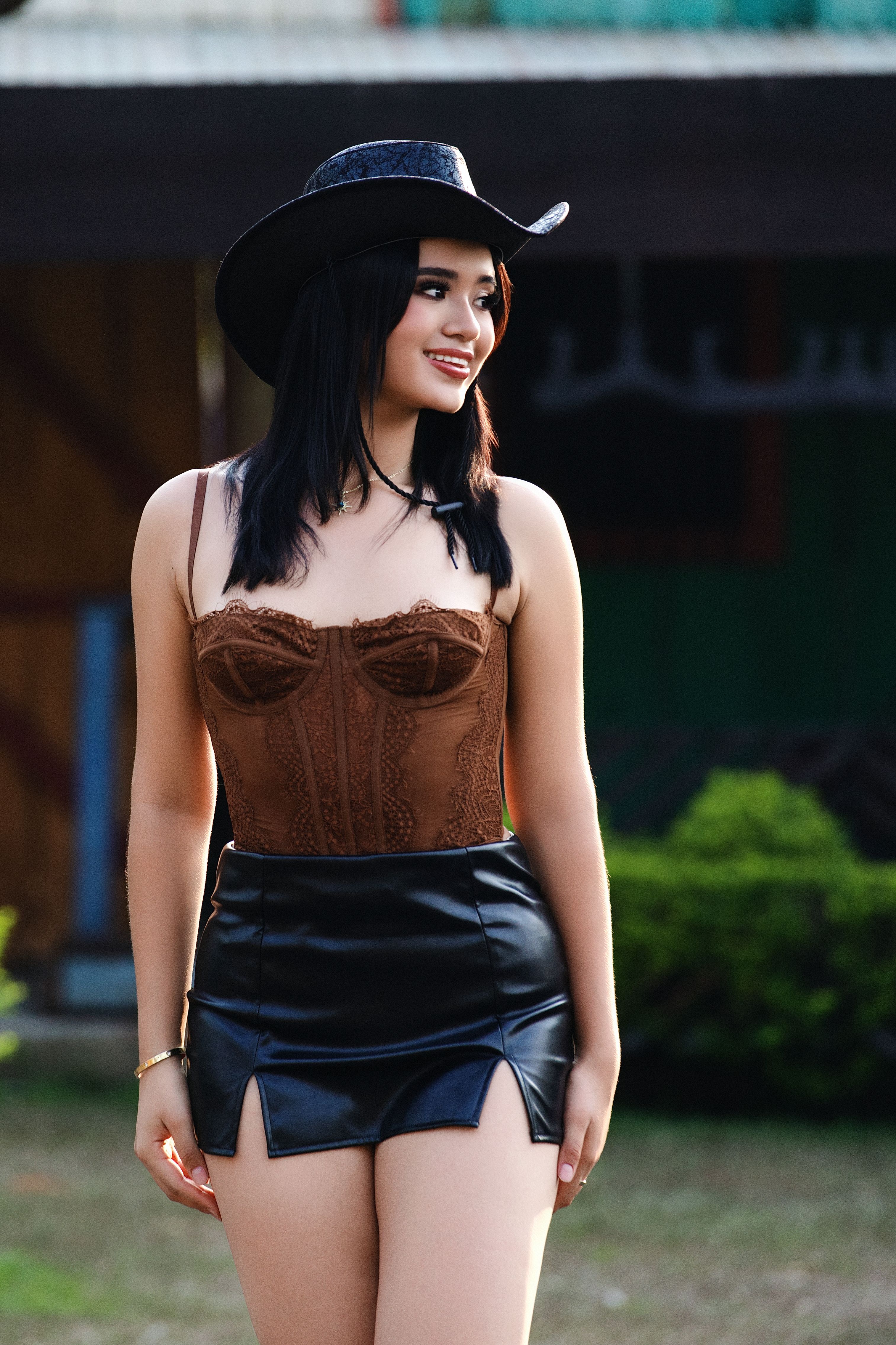 A stylish woman in a cowboy hat and leather skirt poses outdoors.