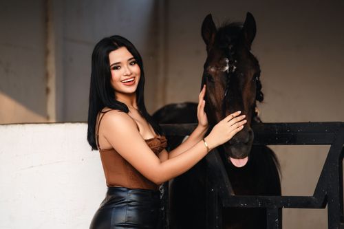 Free A cheerful woman in stylish attire poses indoors with a friendly horse, showcasing a bond between human and animal. Stock Photo