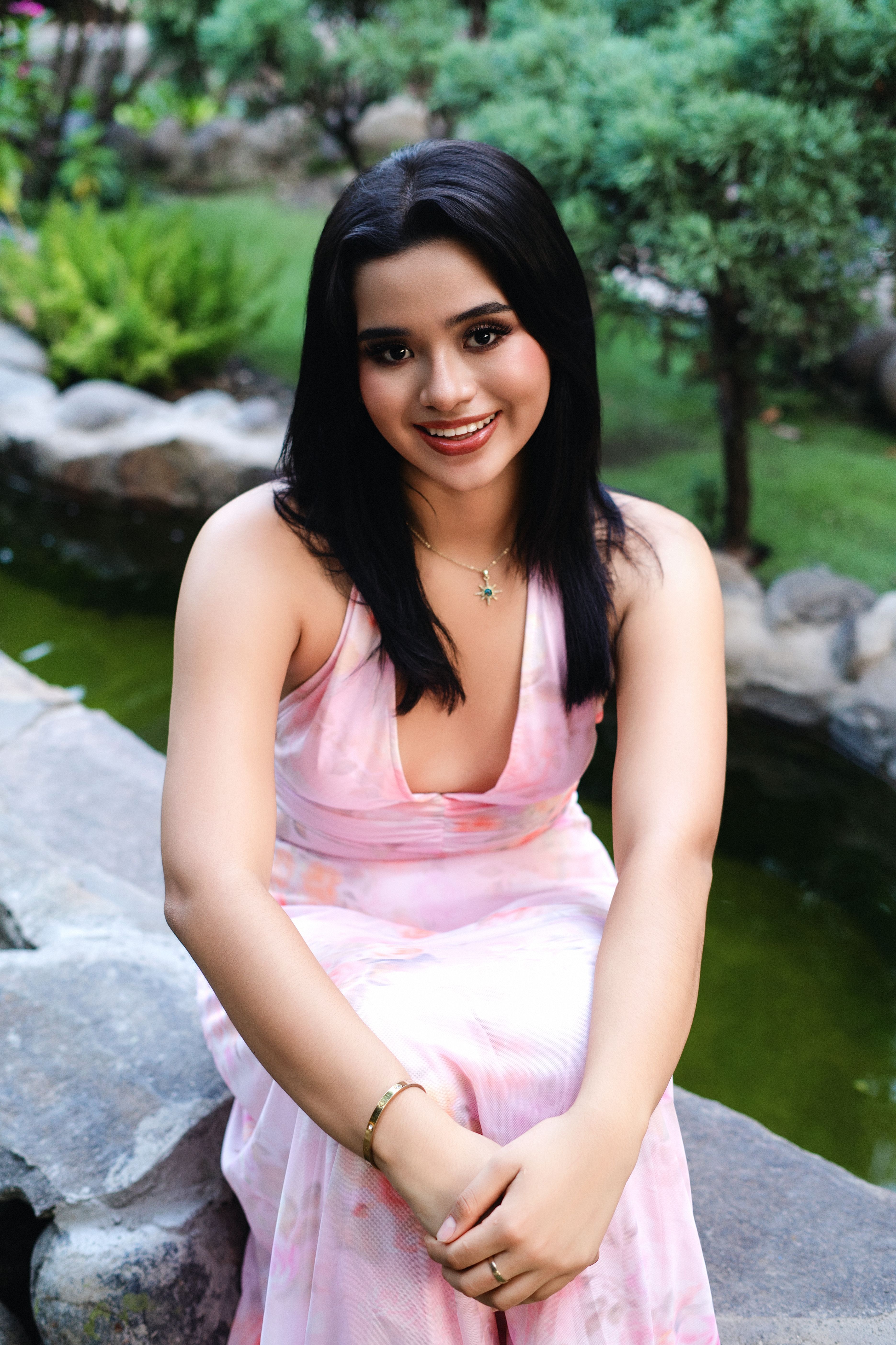 Smiling woman in pink dress enjoying a peaceful garden setting outdoors.