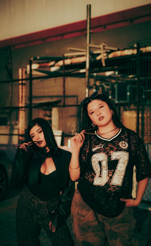 Free Two women in trendy streetwear pose confidently in an industrial setting at sunset. Stock Photo