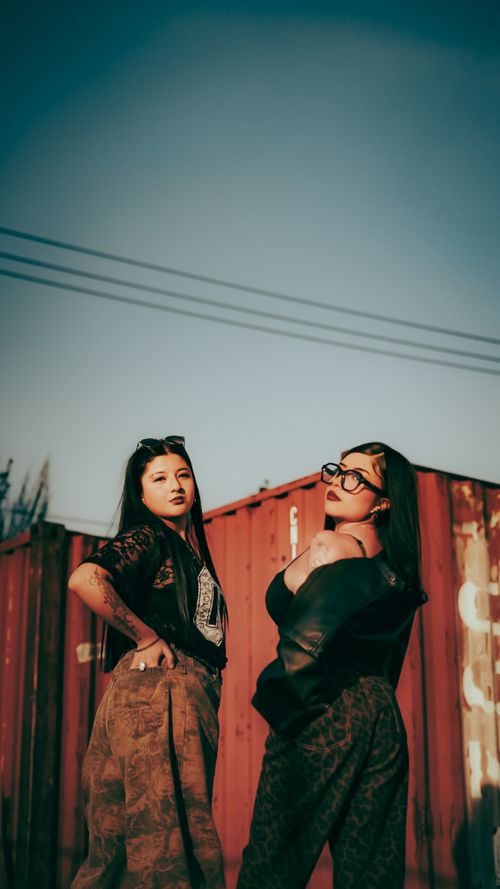 Free Two fashionable women in trendy outfits and sunglasses pose confidently outdoors in front of shipping containers. Stock Photo