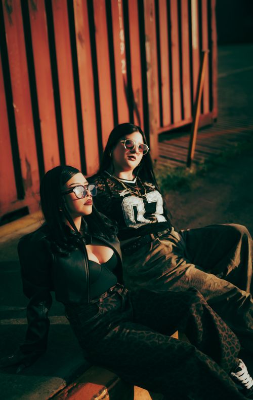Free Two stylish women in sunglasses lounging by a rust-colored container in an urban setting. Stock Photo