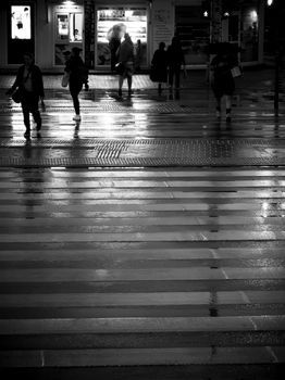 Black and white of people crossing wet street in Wrocław at night.