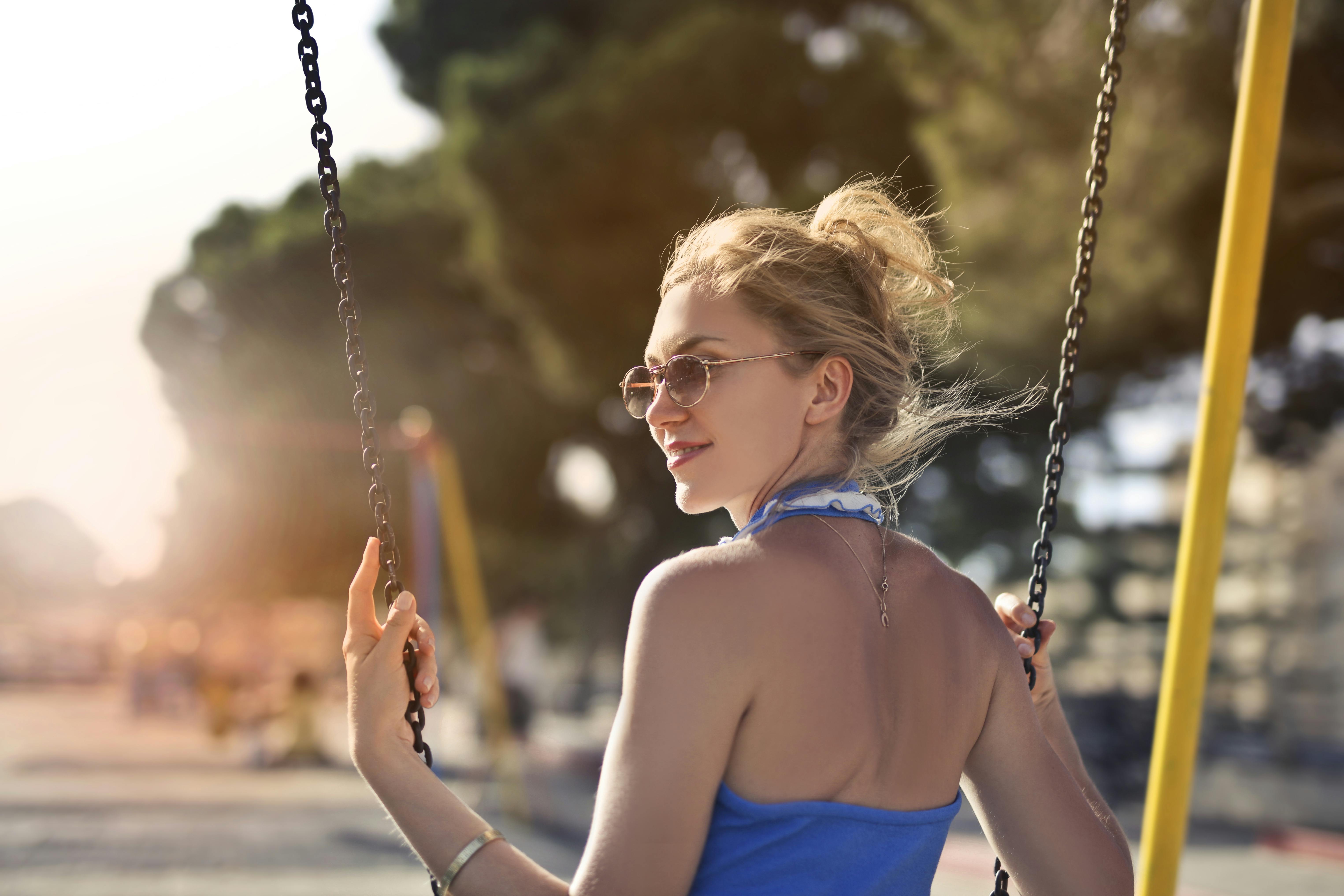 一位美丽的金发女子戴着墨镜，在秋千上享受着阳光明媚的一天