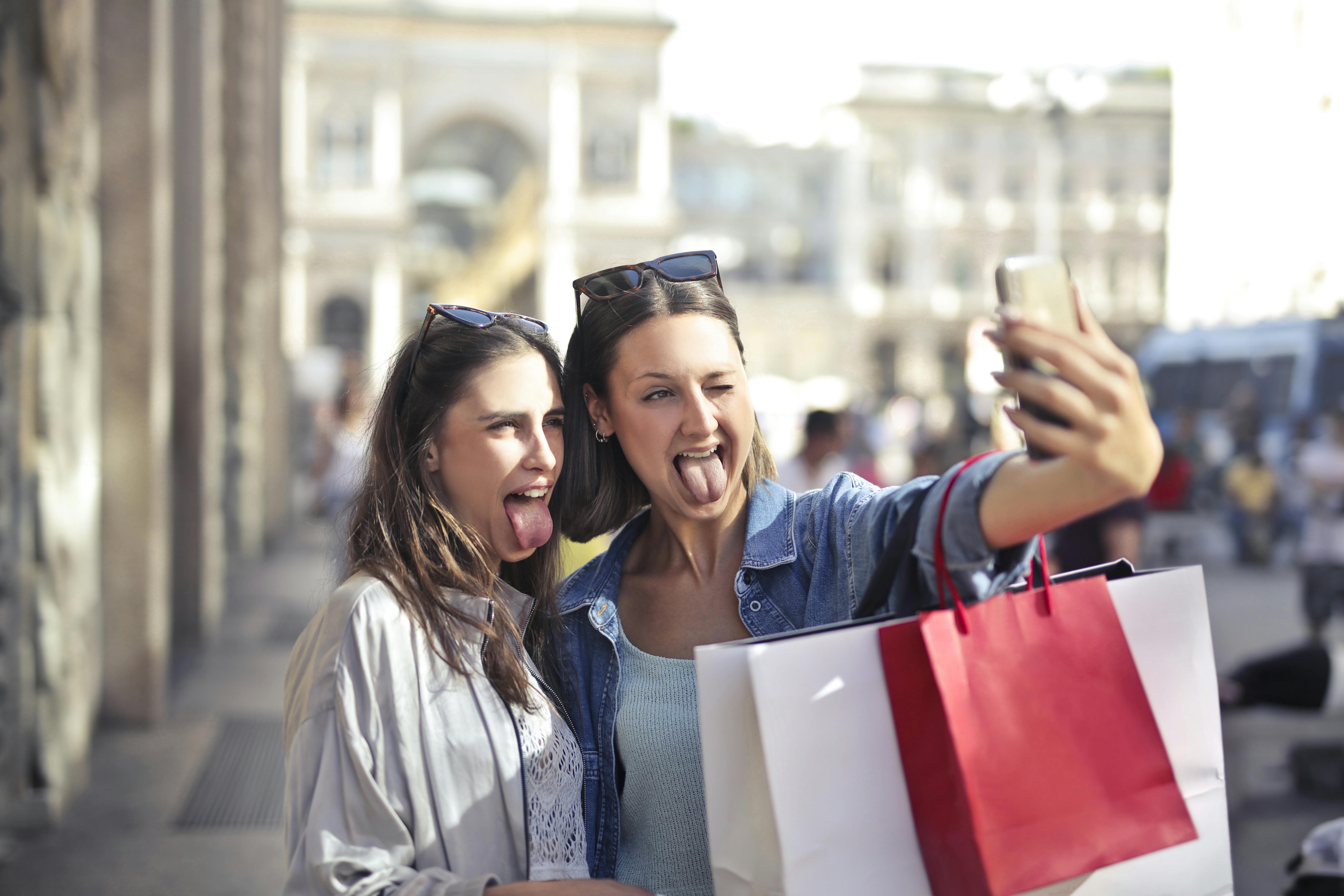 cheerful young women with shopping bags taking selfie on street