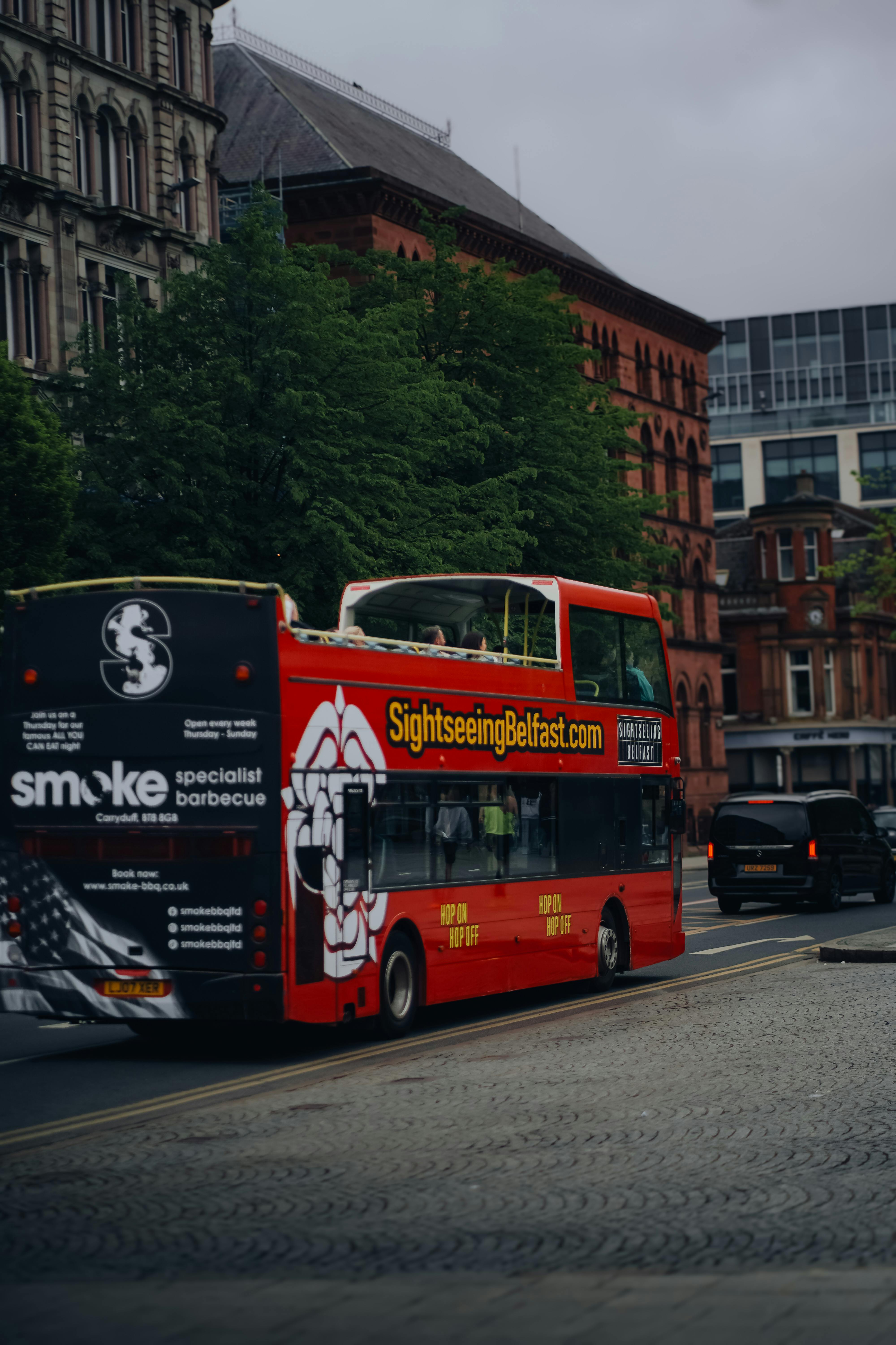 A vibrant sightseeing bus travels through a historic street in Belfast, Northern Ireland.