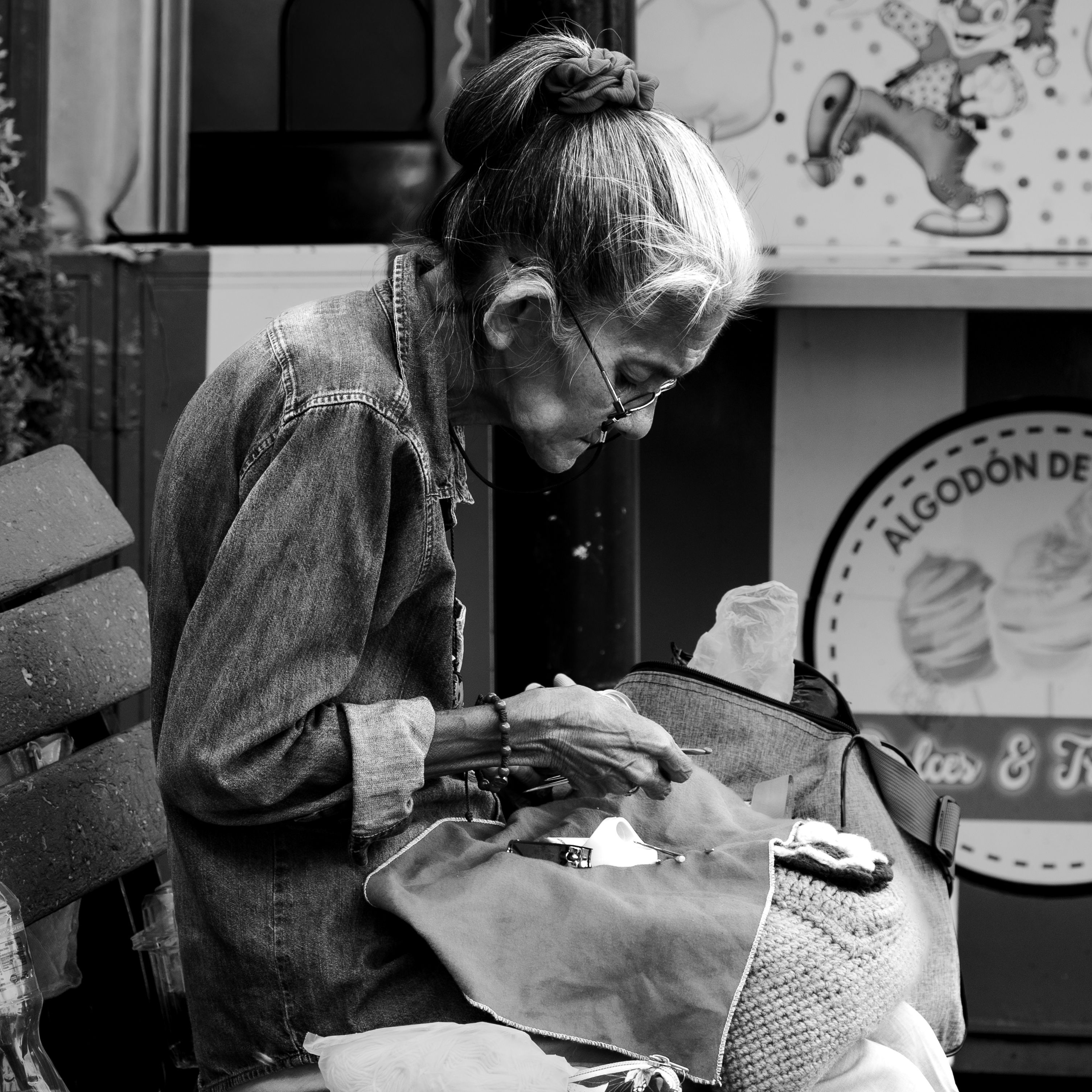 An elderly woman focused on sewing while seated on a park bench in Guayaquil, Ecuador.