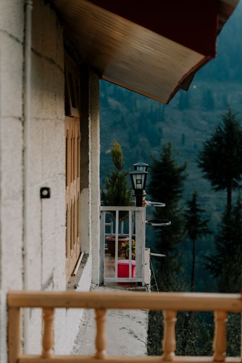Free A serene balcony view from a rustic home overlooking lush green mountains in Himachal Pradesh. Stock Photo
