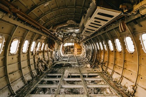 Free Interior of old airplane cabin after having accident made of metal beams and rounded windows with luggage rack in daylight Stock Photo