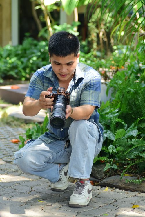 Free A young male photographer kneels and takes a photo in a lush outdoor setting. Casual and focused. Stock Photo