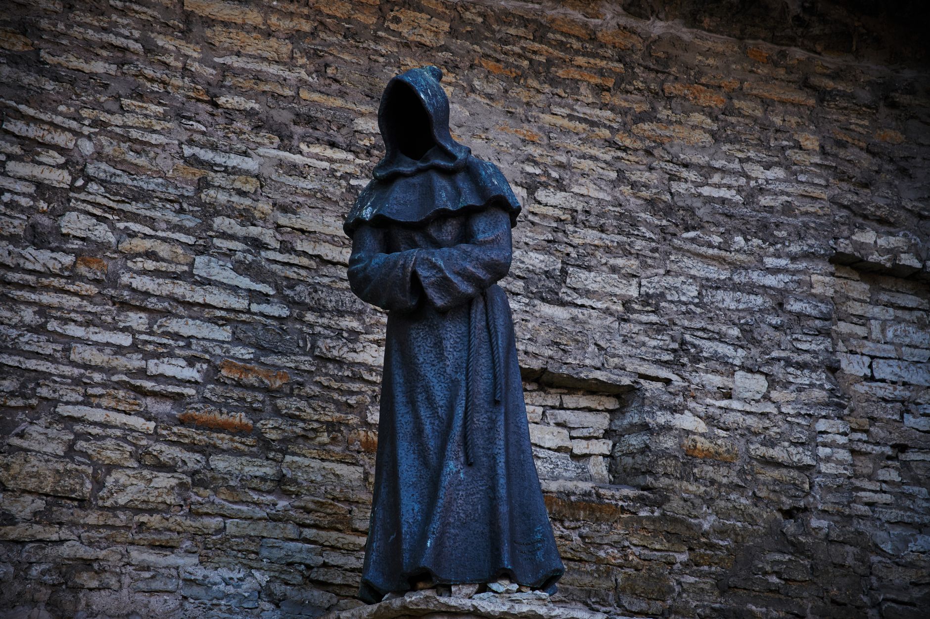 Explore this eerie hooded figure sculpture in Tallinn's historic old town, set against ancient stone walls.