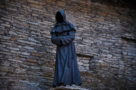 Explore this eerie hooded figure sculpture in Tallinn's historic old town, set against ancient stone walls.