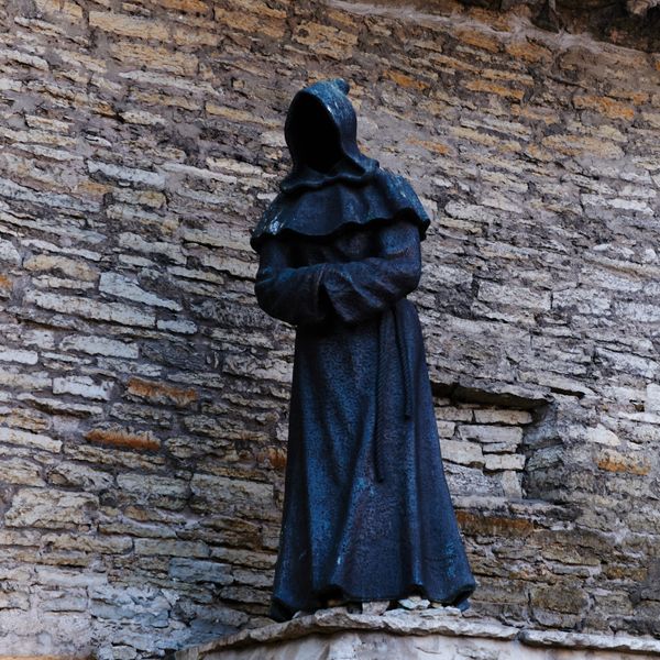 Hooded figure sculpture against a rustic stone wall — photo by Nils Rotura on Pexels
