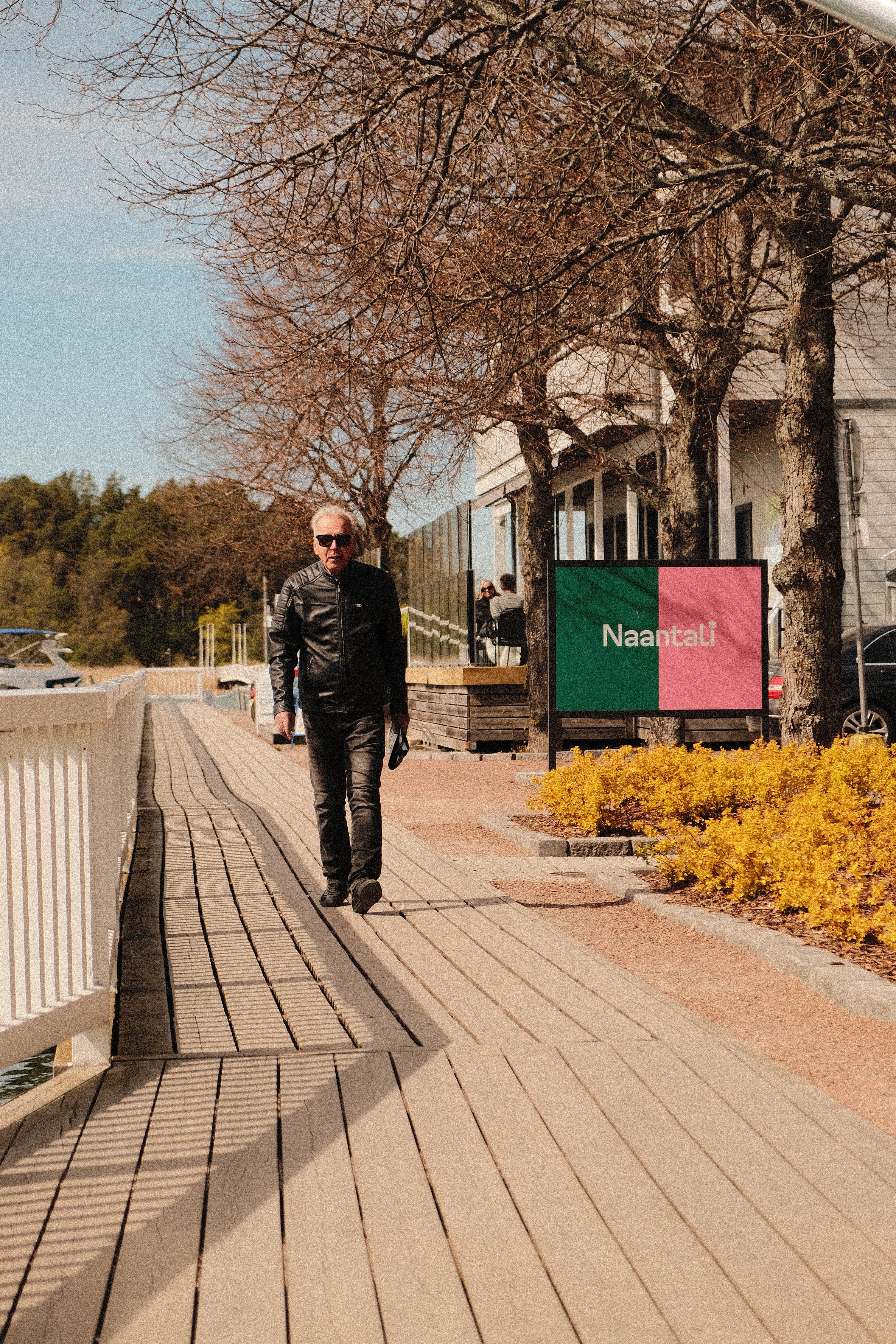 A stylish man walks along a scenic boardwalk in Naantali, Finland on a sunny day.