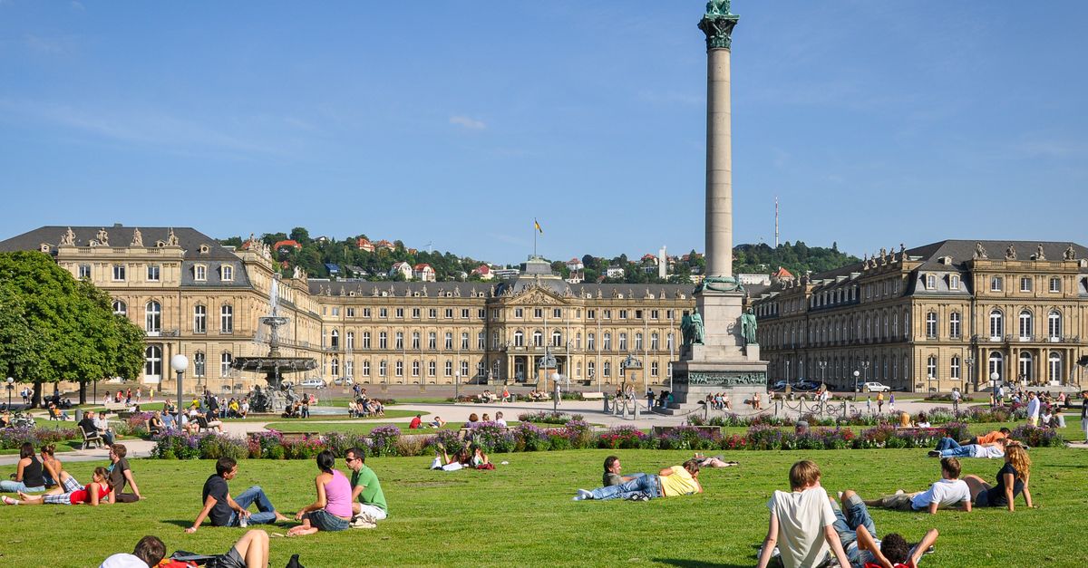 People relaxing on the grass at Schlossplatz, Stuttgart, under a sunny sky with Neues Schloss in the background.