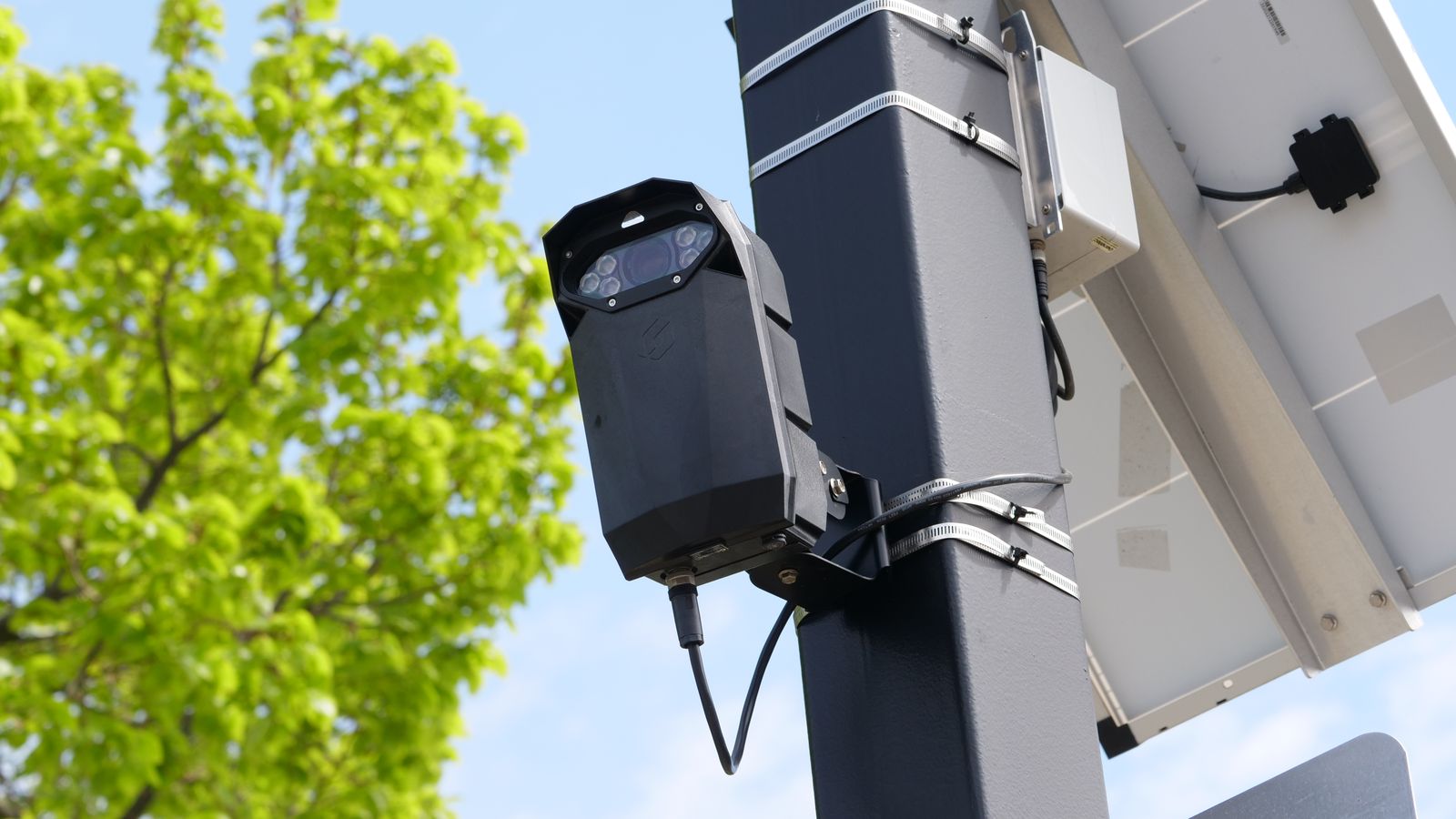A modern surveillance camera powered by solar energy mounted on a street pole.