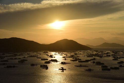 Free Golden sunset over bay with silhouetted mountains and floating structures, creating a tranquil, serene scene. Stock Photo