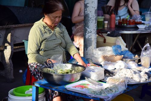 Free Elderly woman at an outdoor street food market preparing delicious traditional dishes. Stock Photo