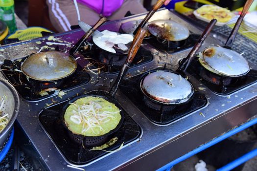 Close-up of a street food vendor preparing savory pancakes on a griddle outdoors.