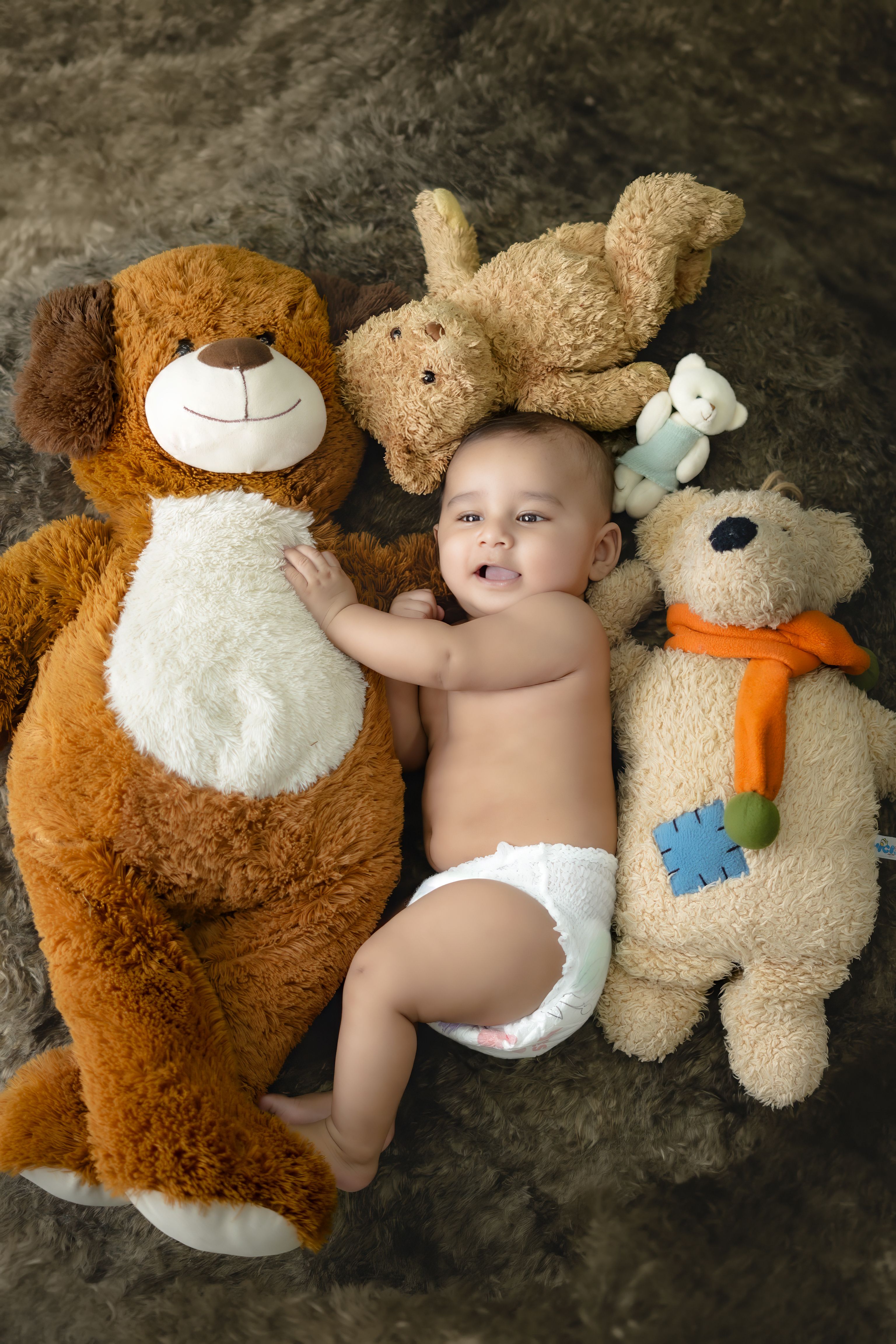 Cute baby lying among cuddly bear stuffed animals creating a cozy scene.