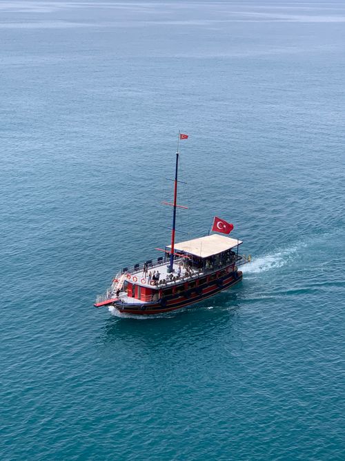 Free A traditional boat with Turkish flags sails through Antalya's vibrant blue waters, showcasing maritime culture. Stock Photo