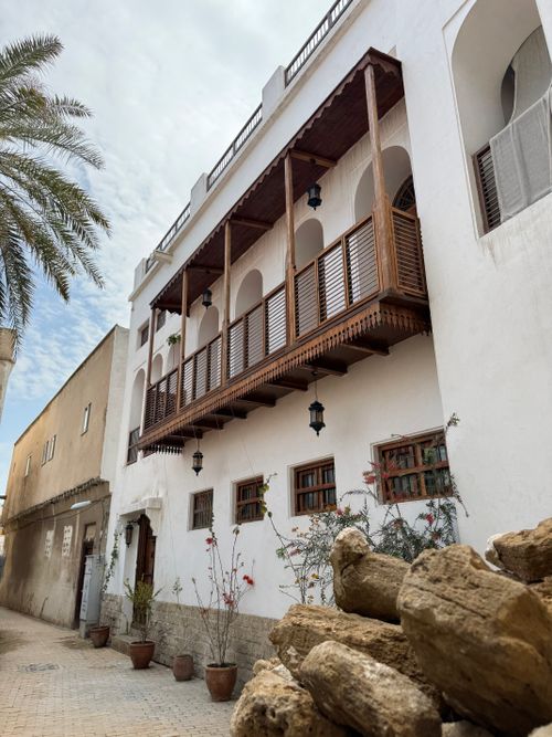 Free Charming Middle Eastern building with wooden balcony and palm tree accents in a sunny, serene street. Stock Photo