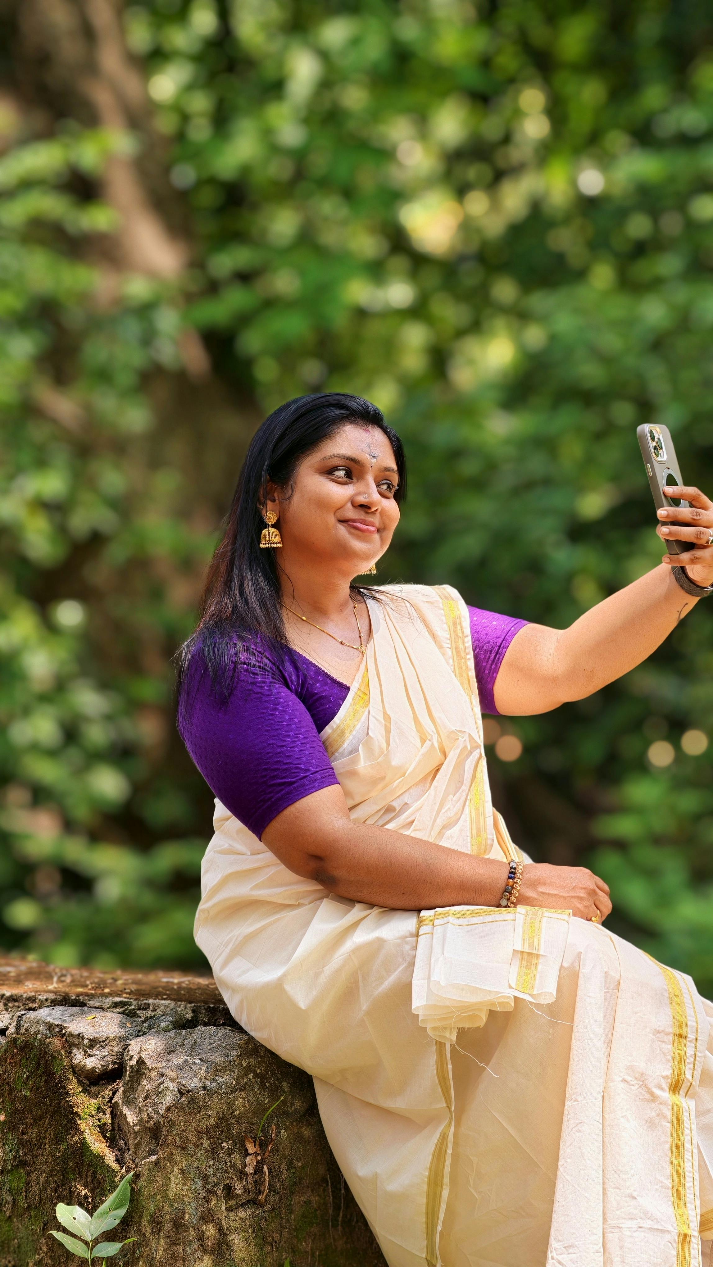South Asian woman in a saree taking a selfie outdoors, blending tradition with technology.