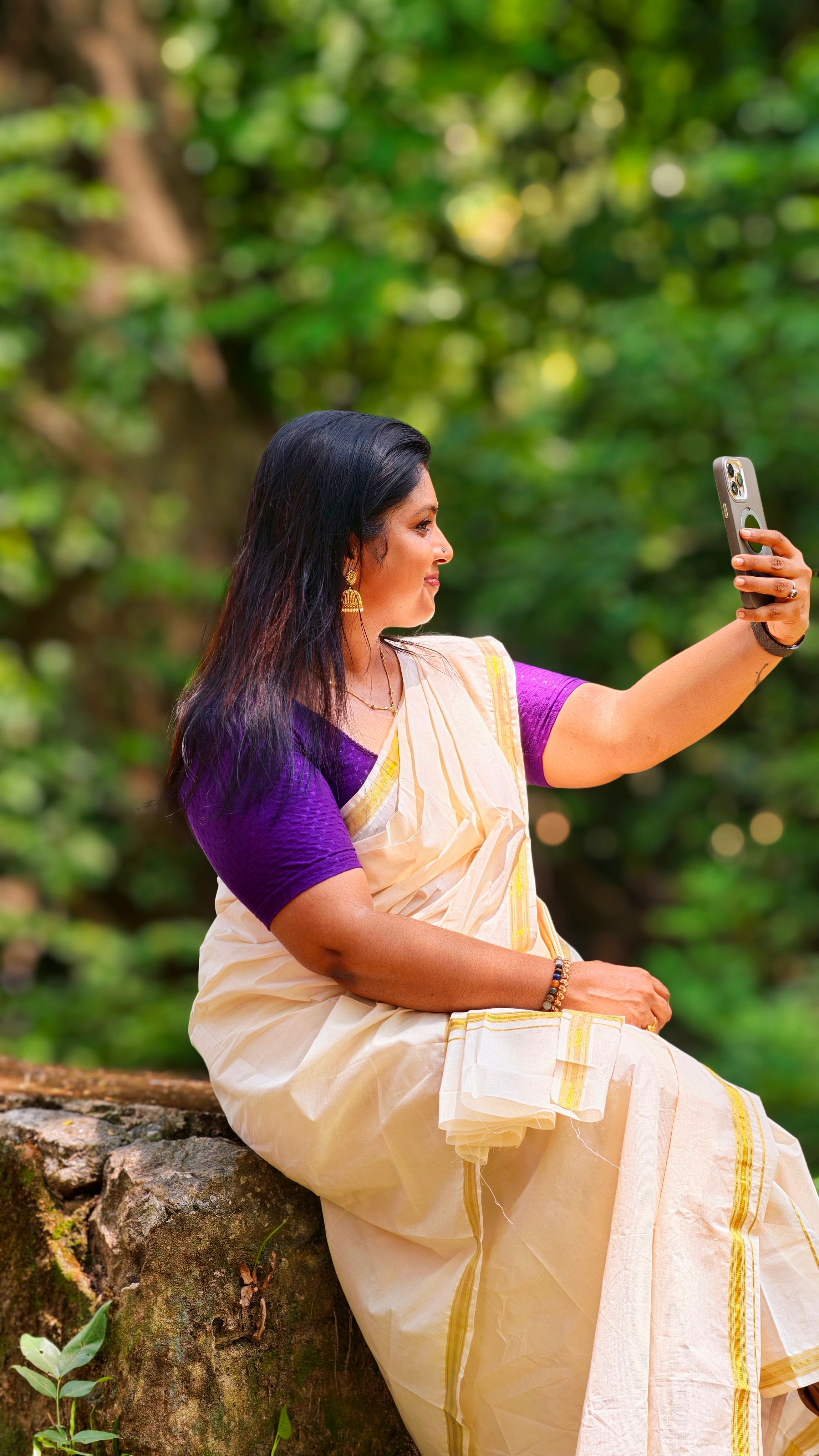 A South Indian woman in a saree takes a selfie outdoors, blending tradition with technology.